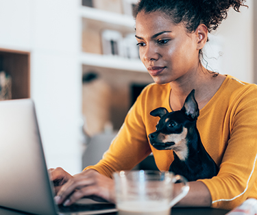 Uma mujer con su pequeño perro escribiendo en su computadora portatil