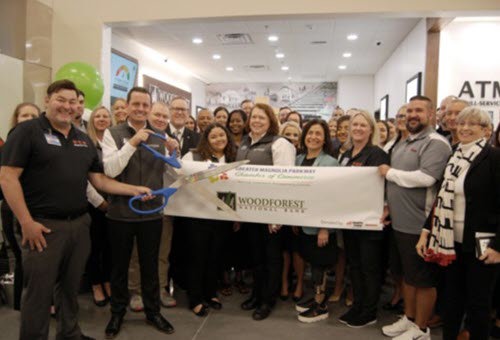 Officiating the ribbon cutting ceremony are Woodforest’s Brett Simms, Assistant VP & Branch Manager (holding scissors) and Julie Mayrant, President & Chief Retail Officer (4th from right, front row), with H-E-B store manager John Beardsley (far left) and Sandy Barton, President of the Greater Magnolia Parkway Chamber of Commerce (far right).